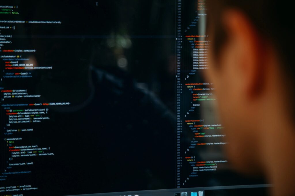 The blurred side of a man's head as he looks at a split screen of coding.