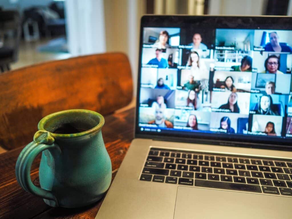 A laptop screen with a zoom meeting on it. A green coffee mug sits beside the computer.