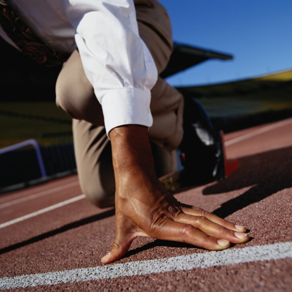 A man's black hand braced on the ground of a running track.