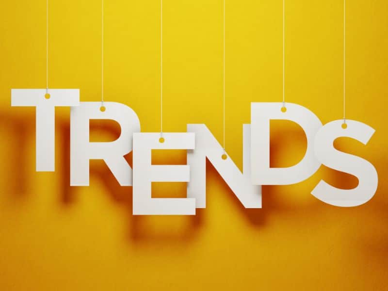 Big, white paper letters hanging from strings in front of a yellow wall spelling the word "TRENDS."