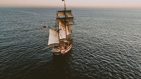 A wooden sailing ship in the middle of the ocean, flying the American flag.
