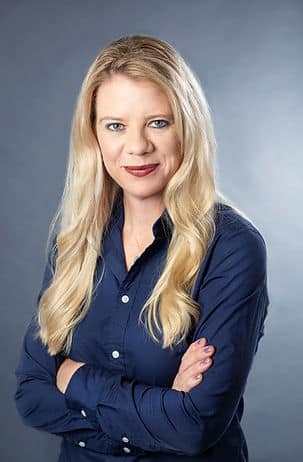 A headshot of a blonde woman wearing a navy button-up.
