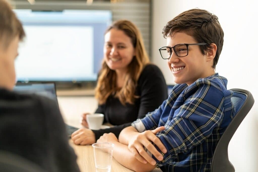 A smiling intern with glasses talks to colleagues in the office.