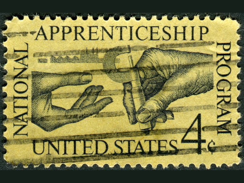 A yellowed apprenticeship stamp depicting two hands, one handing a key to the other. It says "National Apprenticeship Program United States 4¢" around the edge.